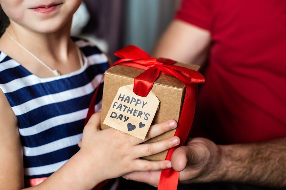 childrens hands give a box with a red bow and a postcard to the mans fathers day daughter gives a gift to dad